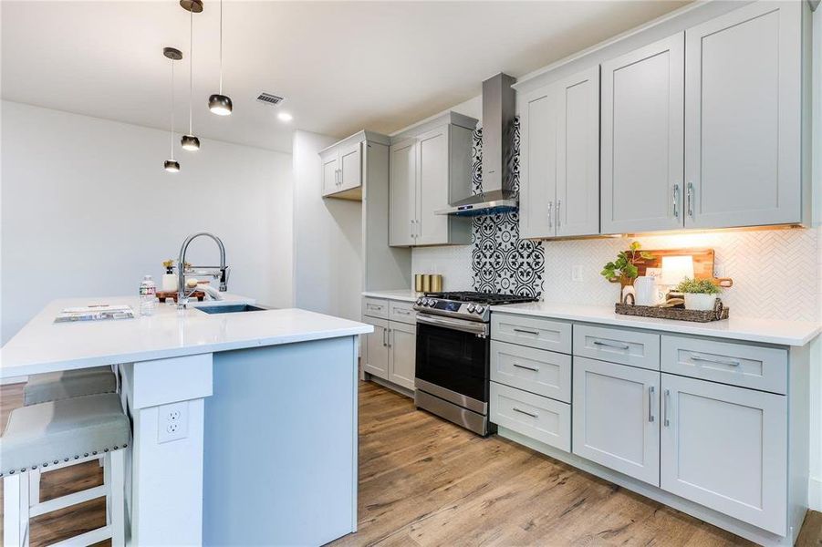 Kitchen featuring pendant lighting, sink, a center island with sink, stainless steel gas range, and wall chimney exhaust hood