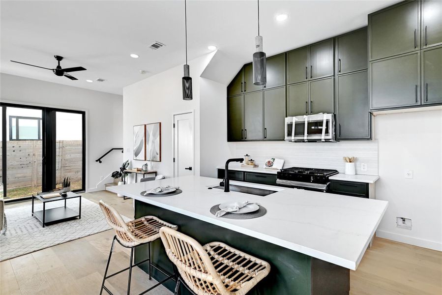 Kitchen with black gas range oven, sink, hanging light fixtures, a breakfast bar, and green cabinets