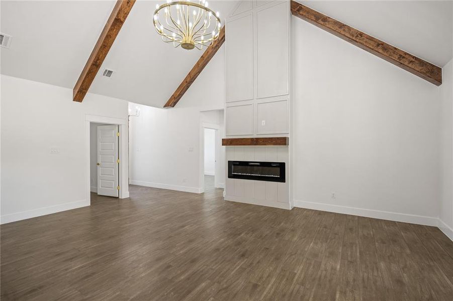 Unfurnished living room featuring a chandelier, lofted ceiling, dark wood finished floors, and a fireplace
