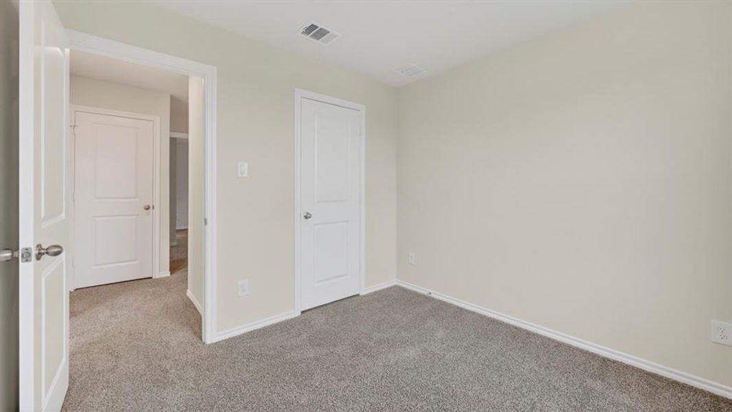 Room featuring light neutral wall paint, gray carpet flooring, white baseboards, and white interior doors with satin nickel hardware