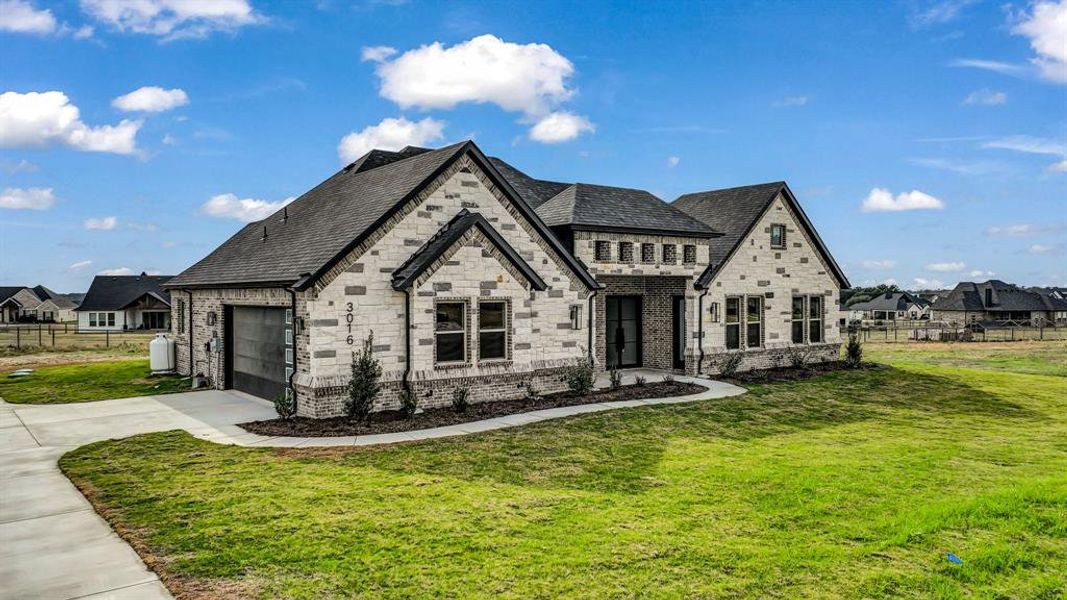 View of front facade featuring concrete driveway, an attached garage, stone siding, and a high end roof