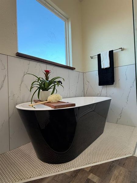 Matte black soaking bathtub for a "me time" placed on white tile for splash zone and stained window.  Custom tile on tile behind bathtub.