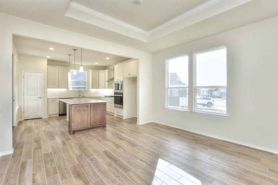 Kitchen with tasteful backsplash, light wood-type flooring, a raised ceiling, and light countertops