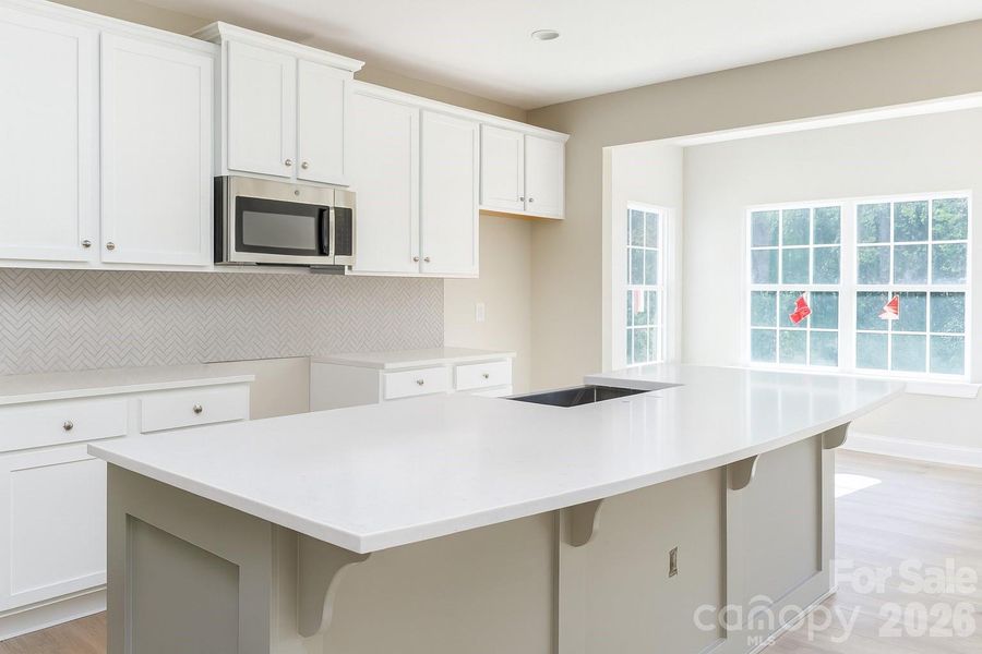 The gourmet kitchen features a spacious island, a farmhouse sink, a gas cooktop, quartz countertops, and a tile backsplash.