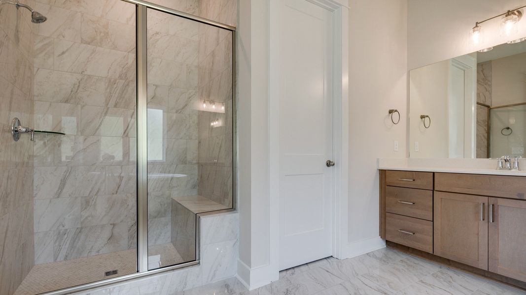 Large tiled primary bathroom with multiple vanities, glass shower enclosure, and freestanding tub