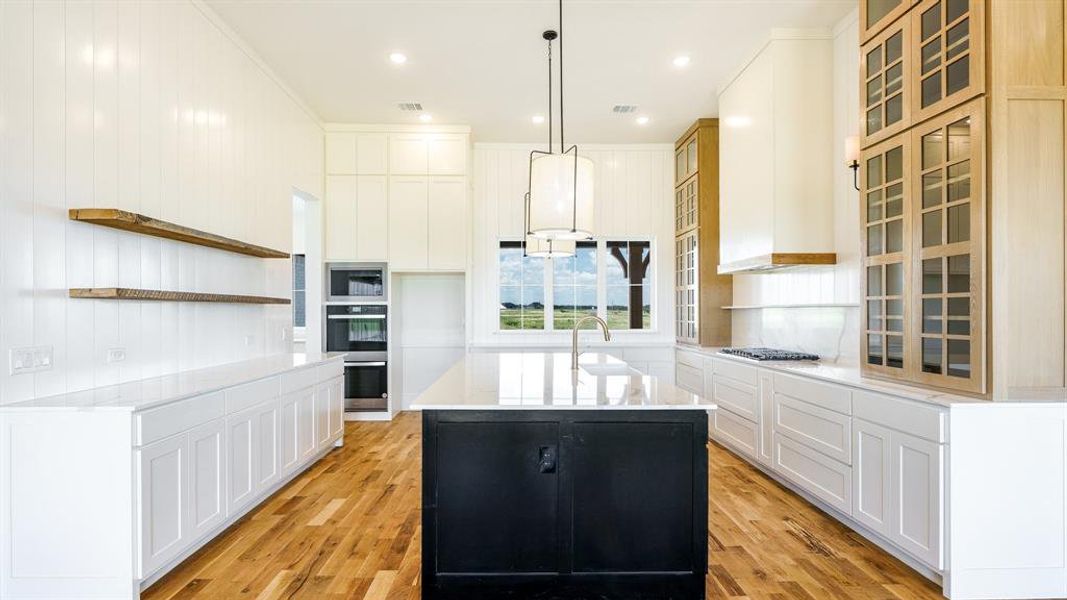 Kitchen featuring appliances with stainless steel finishes, white cabinetry, light hardwood / wood-style floors, decorative light fixtures, and a center island with sink