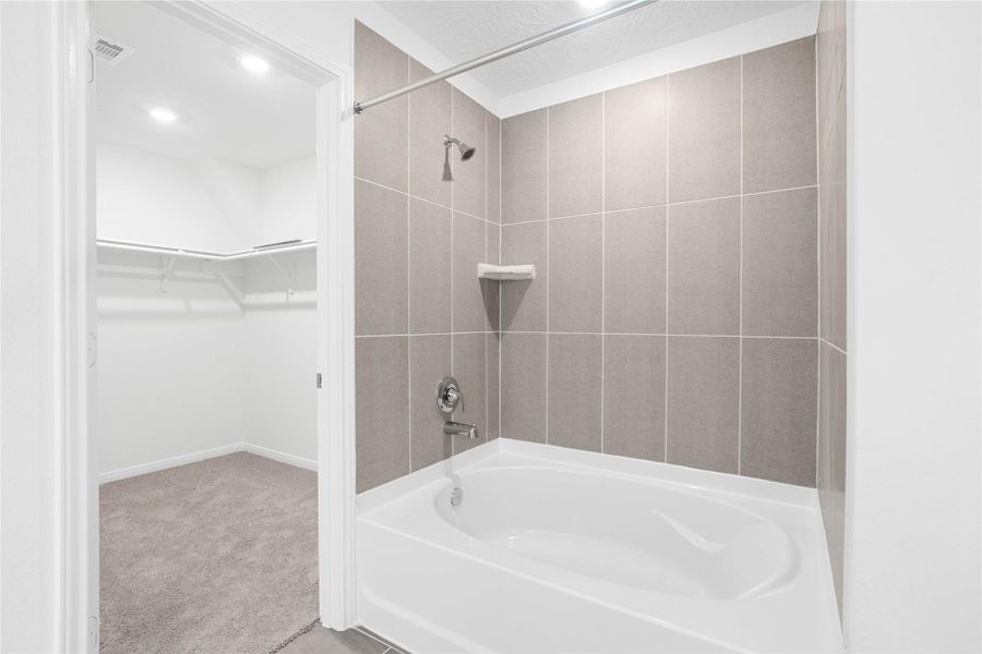 This alternate view of the primary bathroom showcases a large tub/shower combination with tile surround and the walk-in closet!