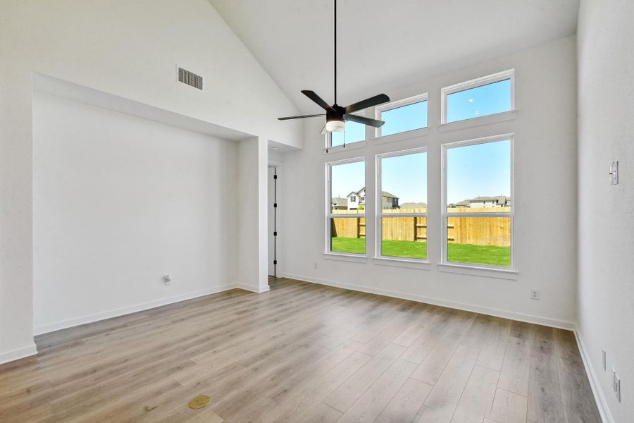 Empty room with ceiling fan, high vaulted ceiling, and wood finished floors