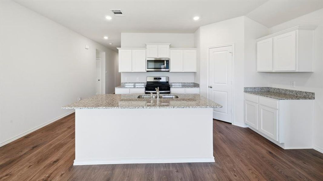 Kitchen with white cabinetry, light stone counters, stainless steel appliances, a center island with sink, and recessed lighting