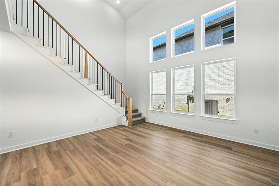 Unfurnished living room with stairway, wood finished floors, plenty of natural light, and a towering ceiling