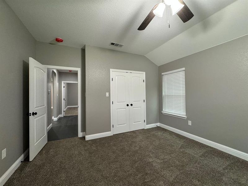 Unfurnished bedroom featuring dark carpet, a textured ceiling, vaulted ceiling, ceiling fan, and a closet