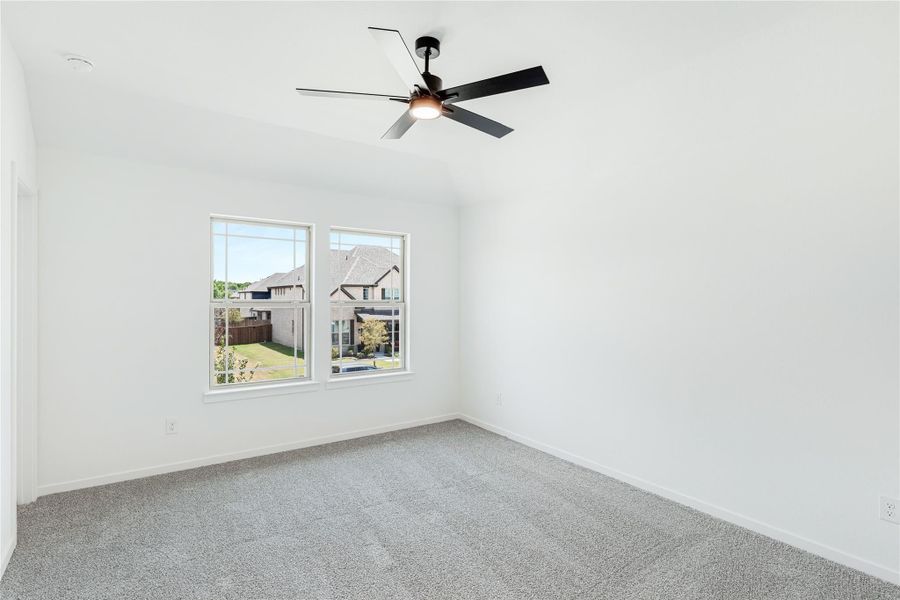 Empty bedroom with gray carpet, ceiling fan, and two windows overlooking neighborhood Empty bedroom with gray carpet, ceiling fan, and two windows overlooking neighborhood