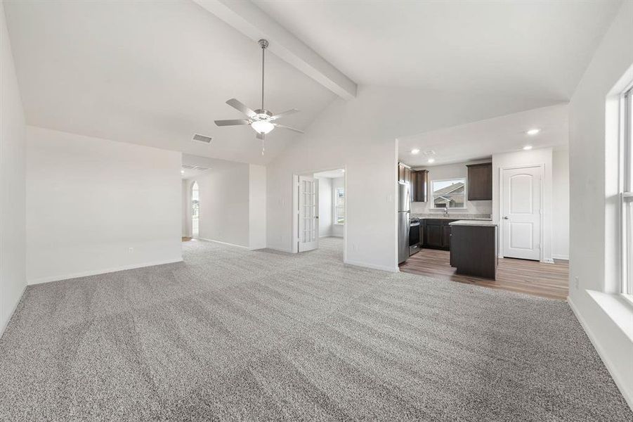 Unfurnished living room featuring sink, beam ceiling, high vaulted ceiling, light carpet, and ceiling fan