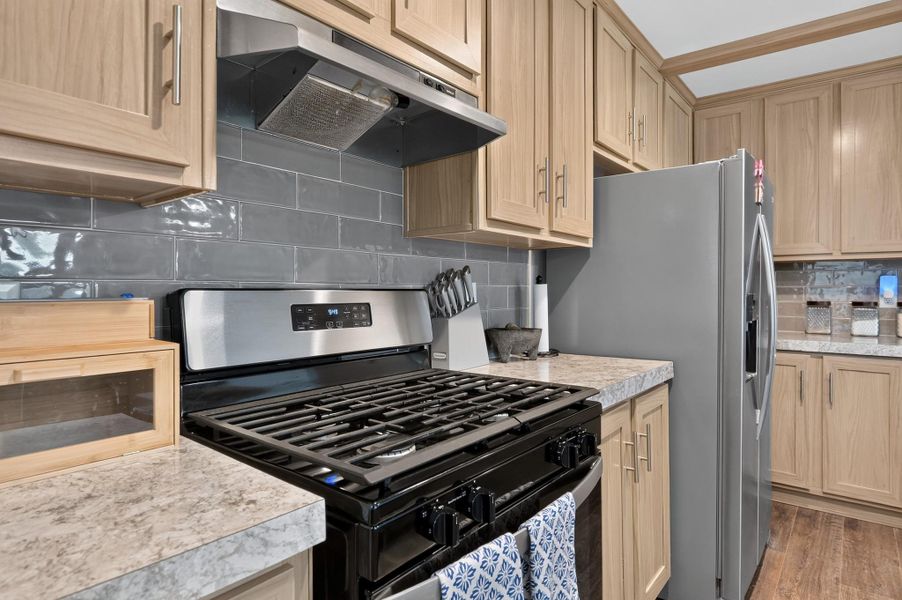 Well-appointed kitchen featuring light wood cabinetry, sleek stainless steel appliances, and contrasting gray subway tile backsplash.