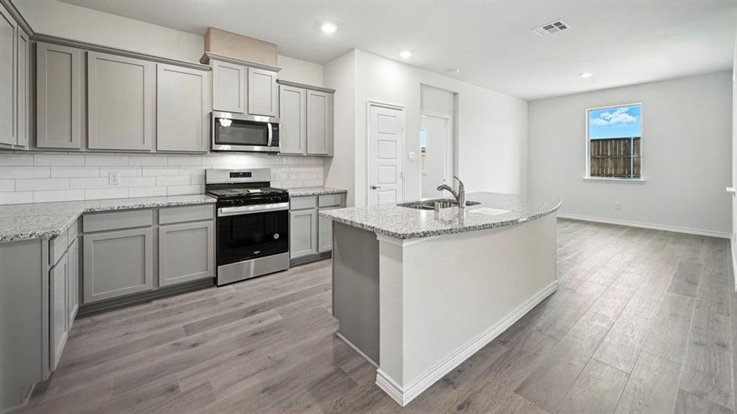 Modern kitchen featuring light gray cabinetry, stainless steel appliances, granite countertops, a white subway tile backsplash, and wood-finish flooring