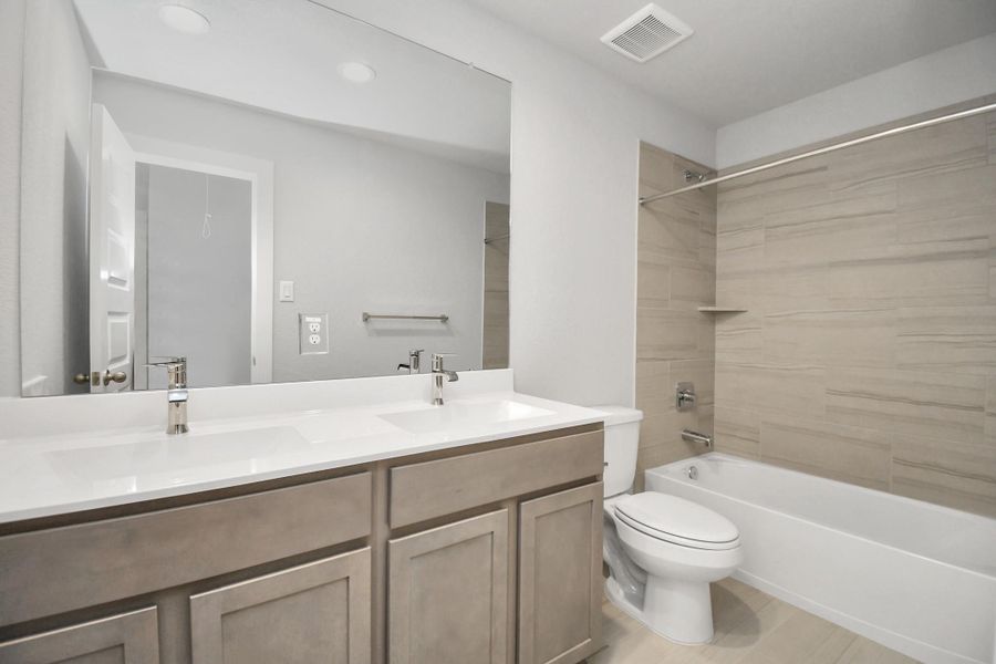 The secondary bath boasts stylish tile flooring, a bath/shower combo with a sleek tile surround, light wood cabinets, and a stunning light countertop. Sample photo of completed home with similar floor plan. Actual colors and selections may vary.