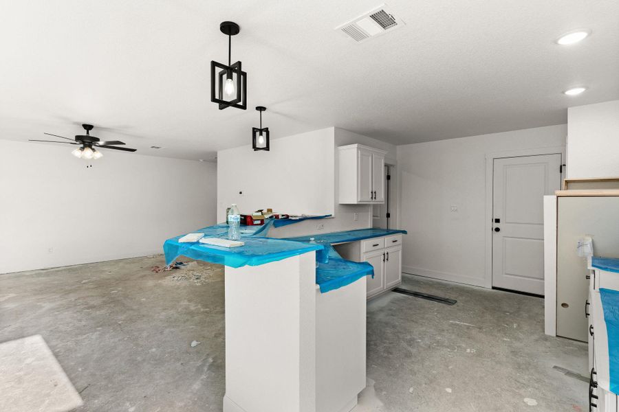 Kitchen with concrete flooring, white cabinetry, a ceiling fan, and hanging light fixtures Kitchen with concrete flooring, white cabinetry, a ceiling fan, and hanging light fixtures