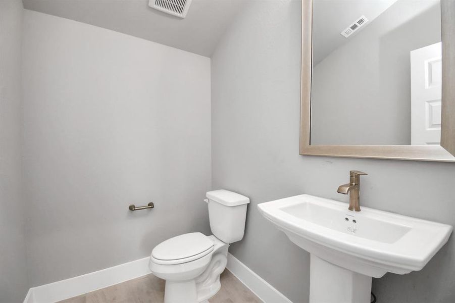 Sophisticated half bathroom adorned in style. Revel in the sleek details, including tile flooring throughout, an upgraded pedestal sink with modern hardware and light fixtures that elevate the elegance of this space. Sample photo of completed home with similar floor plan. Actual colors and selections may vary.