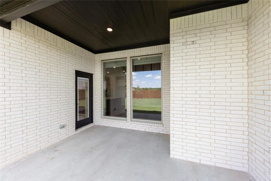 Covered back patio with white brick walls, dark wood ceiling, and sliding glass door to backyard