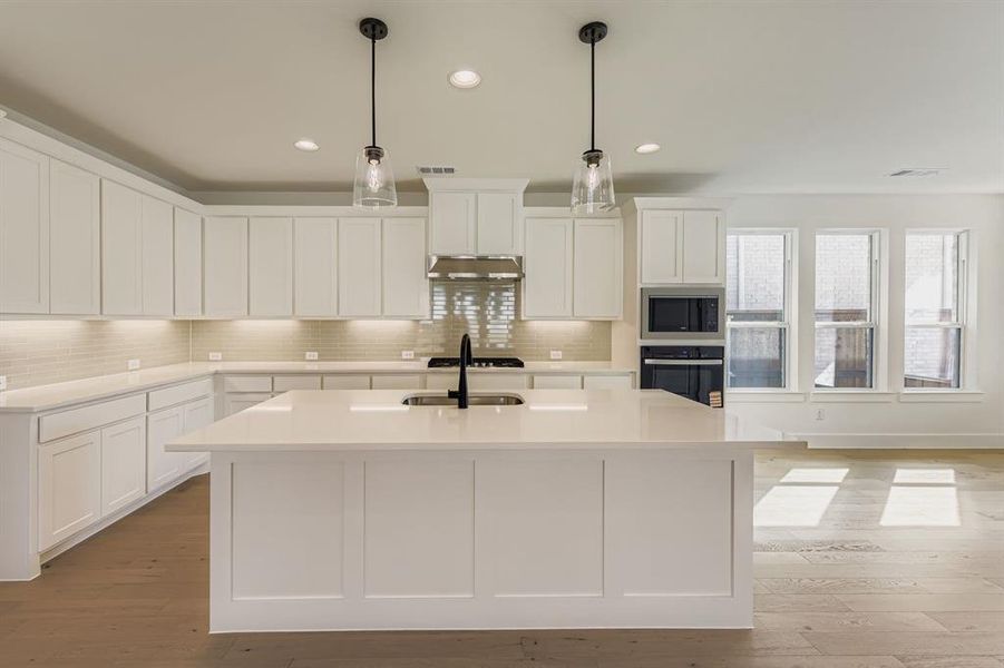 Kitchen featuring tasteful backsplash, white cabinets, light wood-type flooring, a center island with sink, and oven Kitchen featuring tasteful backsplash, white cabinets, light wood-type flooring, a center island with sink, and oven