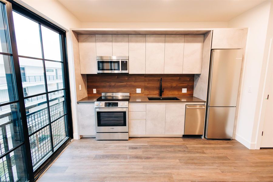 Kitchen featuring appliances with stainless steel finishes, light wood-style floors, tasteful backsplash, and modern cabinets