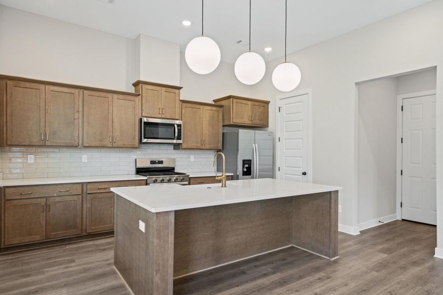 Modern kitchen featuring a central island with a light-toned countertop, wood-finish flooring, recessed lighting, and three spherical pendant lights Modern kitchen featuring a central island with a light-toned countertop, wood-finish flooring, recessed lighting, and three spherical pendant lights