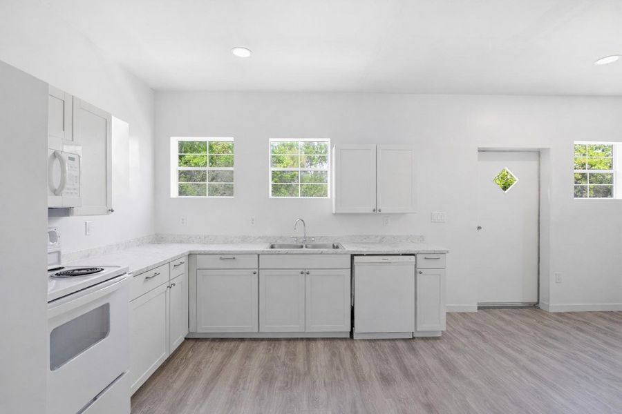 The kitchen features white cabinetry, light-colored countertops, a double basin sink, and a white dishwasher