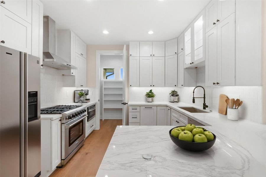 Kitchen featuring a sink, light stone counters, backsplash, wall chimney range hood, and appliances with stainless steel finishes Kitchen featuring a sink, light stone counters, backsplash, wall chimney range hood, and appliances with stainless steel finishes