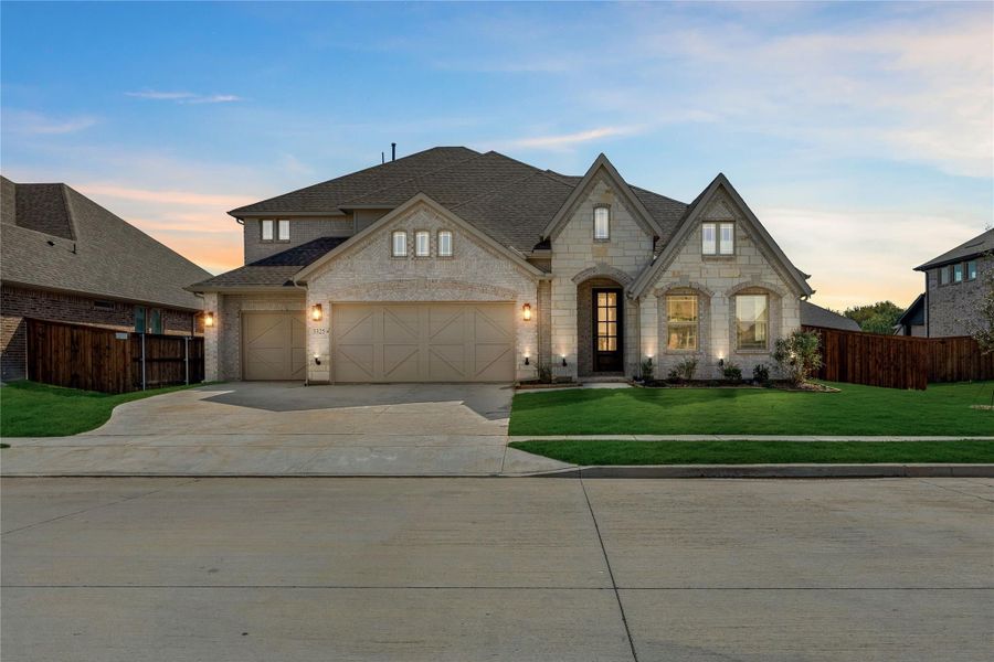 Two-story stone and brick home with three-car garage, arched entry, and manicured front lawn at dusk
