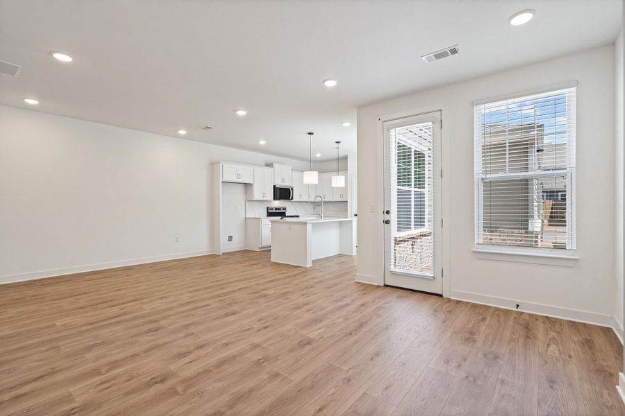 Open-concept living space featuring wood-finish flooring, recessed lighting, and a white kitchen with an island