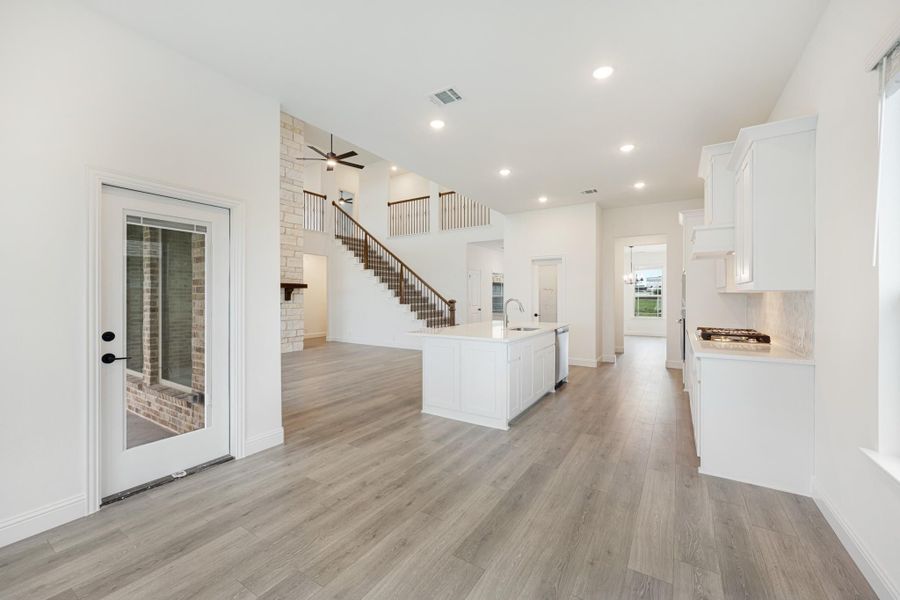 Open-concept kitchen and living area with white island, wood floors, and staircase with second-floor loft visible.