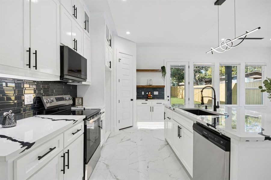Kitchen featuring appliances with stainless steel finishes, decorative backsplash, light stone counters, a kitchen island with sink, and pendant lighting