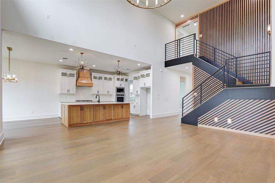 Unfurnished living room featuring a chandelier, stairway, light wood-type flooring, a high ceiling, and recessed lighting