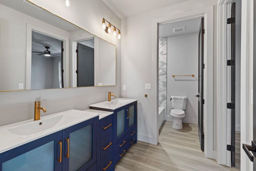 Full bath with double vanity, wood finished floors, visible vents, and a sink