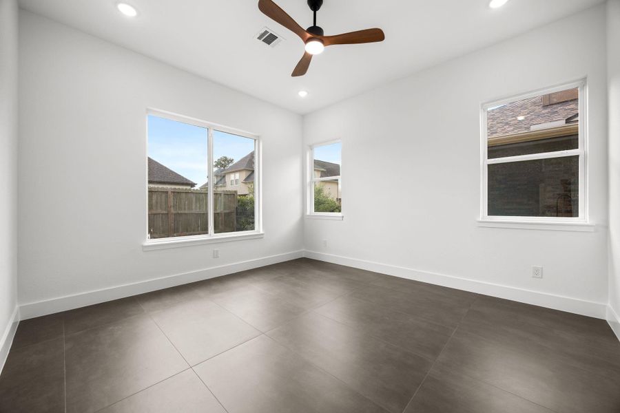 This bright room features large windows, neutral-colored tile flooring, and a ceiling fan, providing a modern and airy feel.