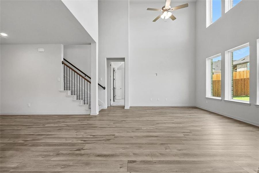 Unfurnished living room with a high ceiling, stairs, ceiling fan, and light wood-style floors Unfurnished living room with a high ceiling, stairs, ceiling fan, and light wood-style floors