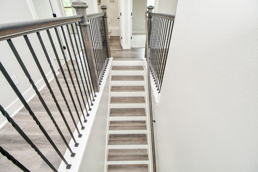 This is a modern staircase with white risers, stylish wood-look treads, and an elegant dark metal baluster railing system, providing a sleek, contemporary transition between floors. This is a modern staircase with white risers, stylish wood-look treads, and an elegant dark metal baluster railing system, providing a sleek, contemporary transition between floors.