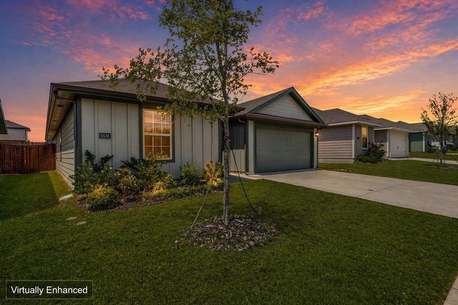 Single-story residence featuring vertical siding, an attached garage, a concrete driveway, and front landscaping with a young tree Single-story residence featuring vertical siding, an attached garage, a concrete driveway, and front landscaping with a young tree