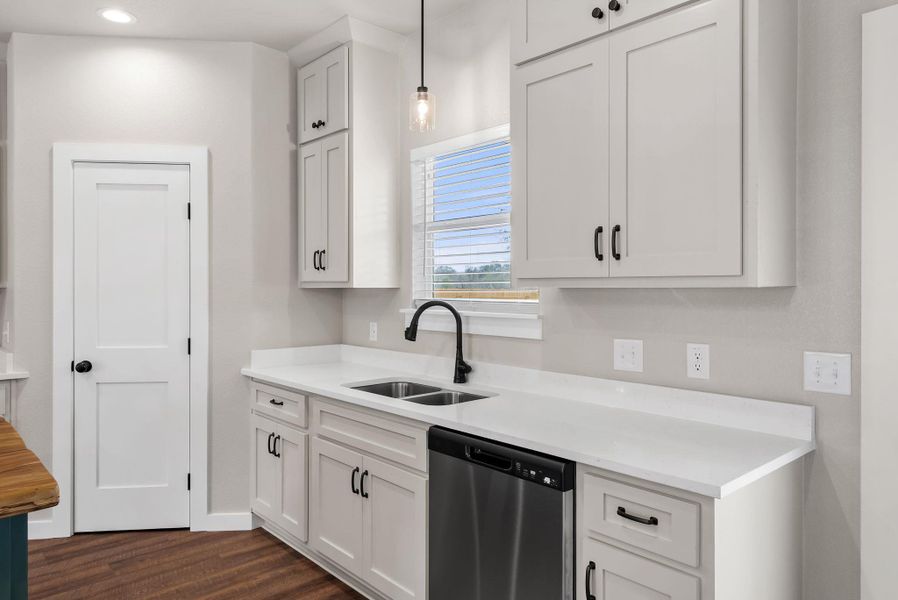 Kitchen featuring dishwasher, white cabinets, decorative light fixtures, and dark wood-style floors