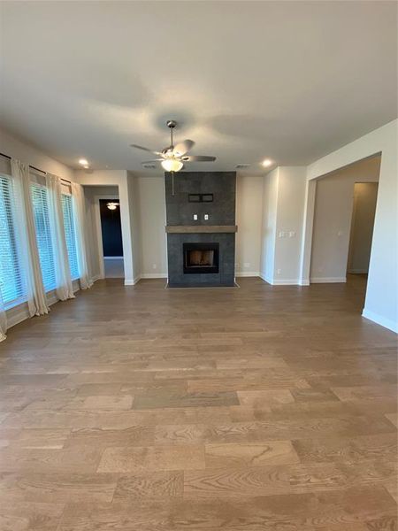 Unfurnished living room featuring a tile fireplace, ceiling fan, and light wood-style floors Unfurnished living room featuring a tile fireplace, ceiling fan, and light wood-style floors