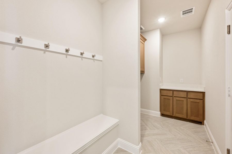 Mudroom with built-in bench, wall hooks, and wood cabinets on tile floor Mudroom with built-in bench, wall hooks, and wood cabinets on tile floor