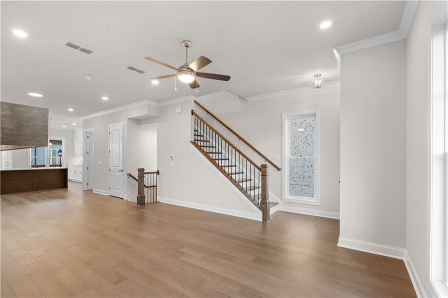 Unfurnished living room featuring recessed lighting, ornamental molding, light wood-type flooring, stairway, and ceiling fan
