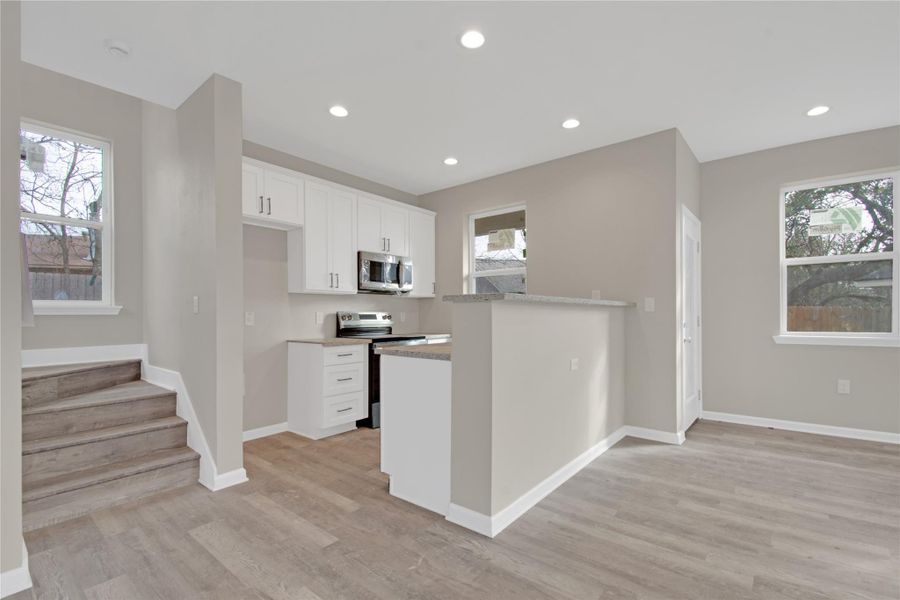 Kitchen with white cabinets, stainless steel appliances, light wood-type flooring, recessed lighting, and light stone countertops