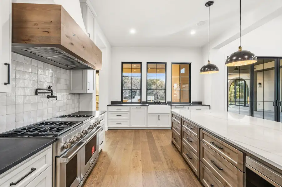 Two tone kitchen with double oven range, dark stone counters, light wood-style flooring, two tone color scheme, and decorative backsplash