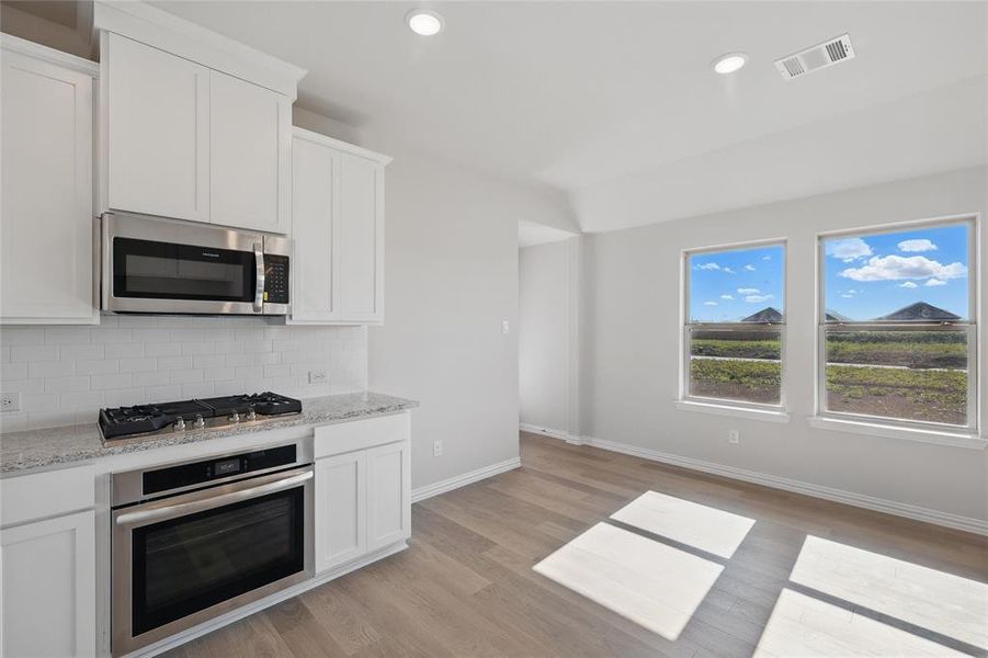 Kitchen featuring appliances with stainless steel finishes, decorative backsplash, light wood-type flooring, white cabinetry, and light stone countertops Kitchen featuring appliances with stainless steel finishes, decorative backsplash, light wood-type flooring, white cabinetry, and light stone countertops