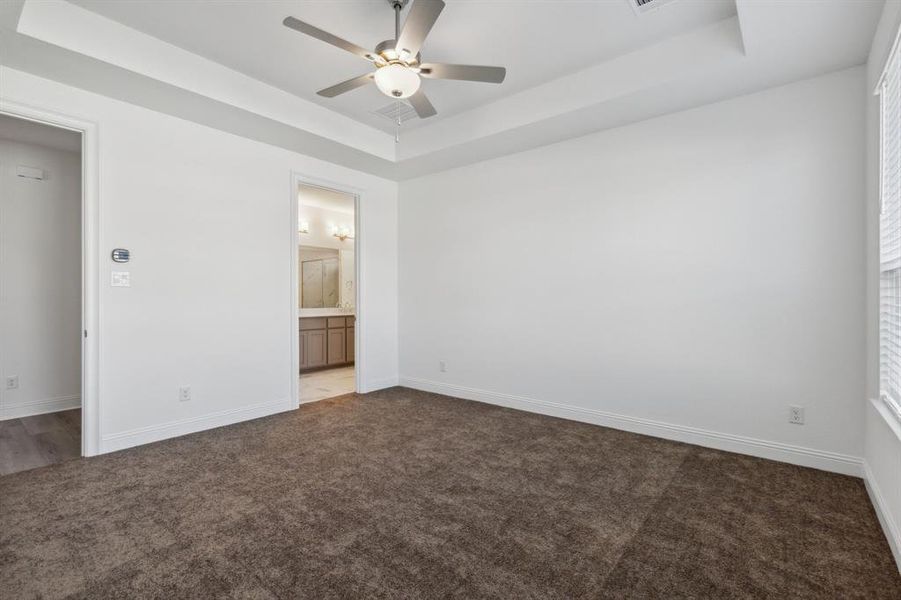 Unfurnished bedroom featuring a tray ceiling, ceiling fan, and ensuite bathroom