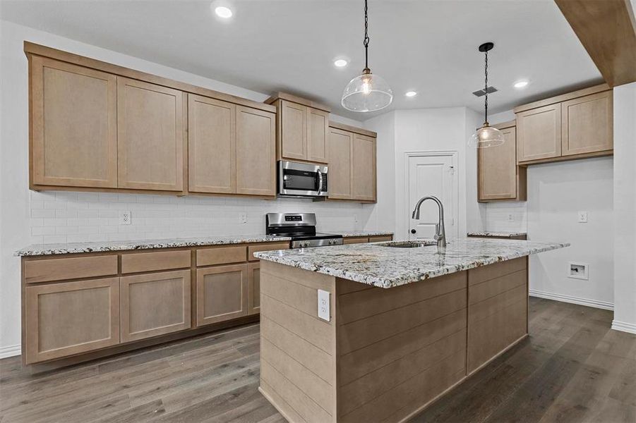 Kitchen with hardwood / wood-style floors, hanging light fixtures, a kitchen island with sink, and stainless steel appliances