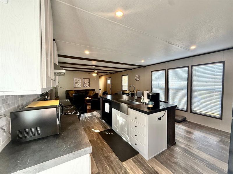 Kitchen featuring white cabinetry, beamed ceiling, stainless steel microwave, dark countertops, and dark wood finished floors