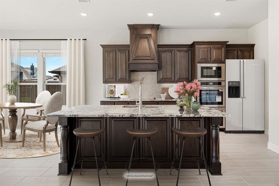 Kitchen with dark wood cabinets, large granite island with three bar stools, and stainless steel appliances