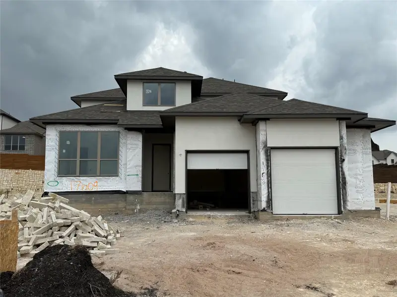 View of front of home with an attached garage, a shingled roof, and stucco siding
